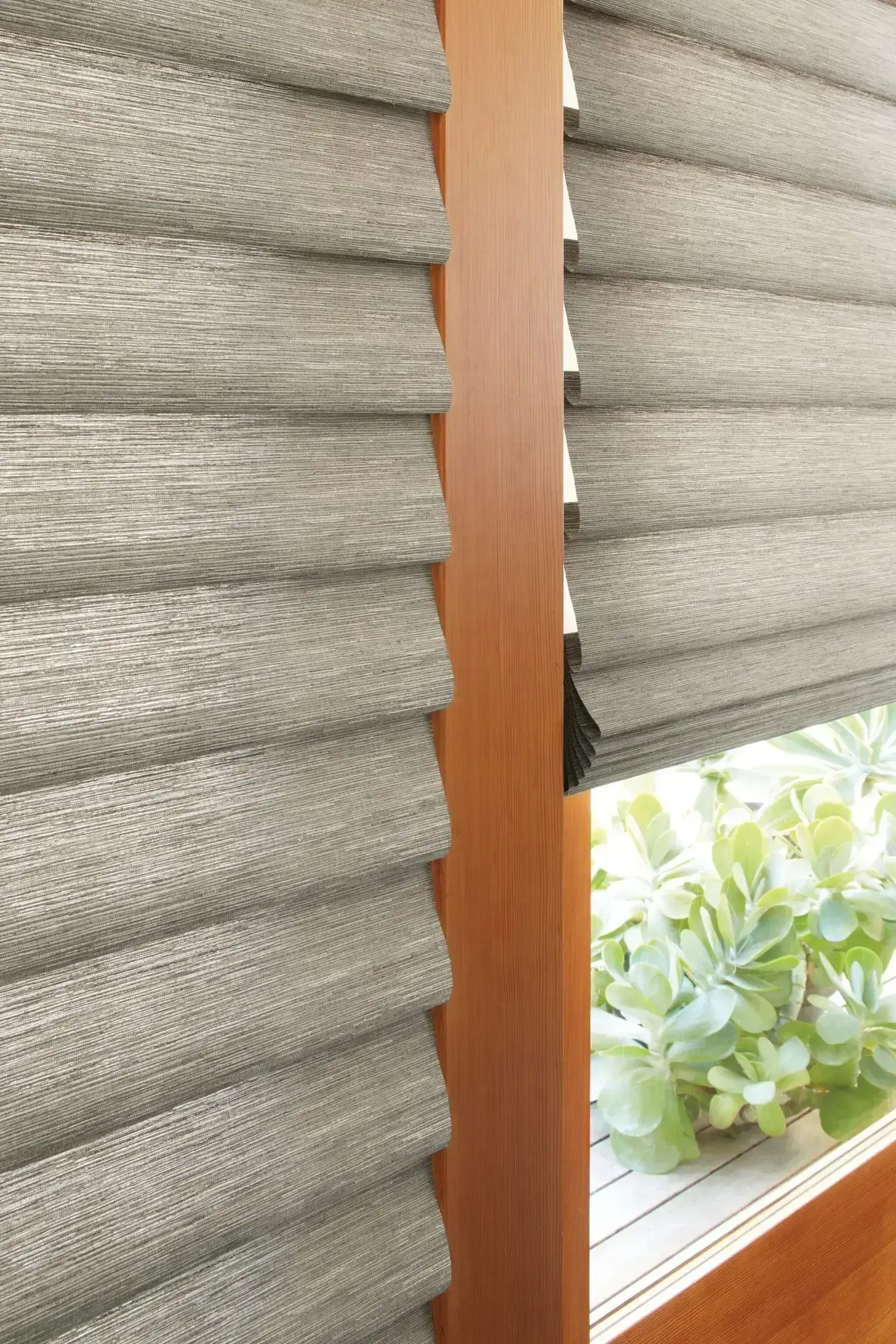 Modern textured window blinds partially covering a window with a wooden frame.